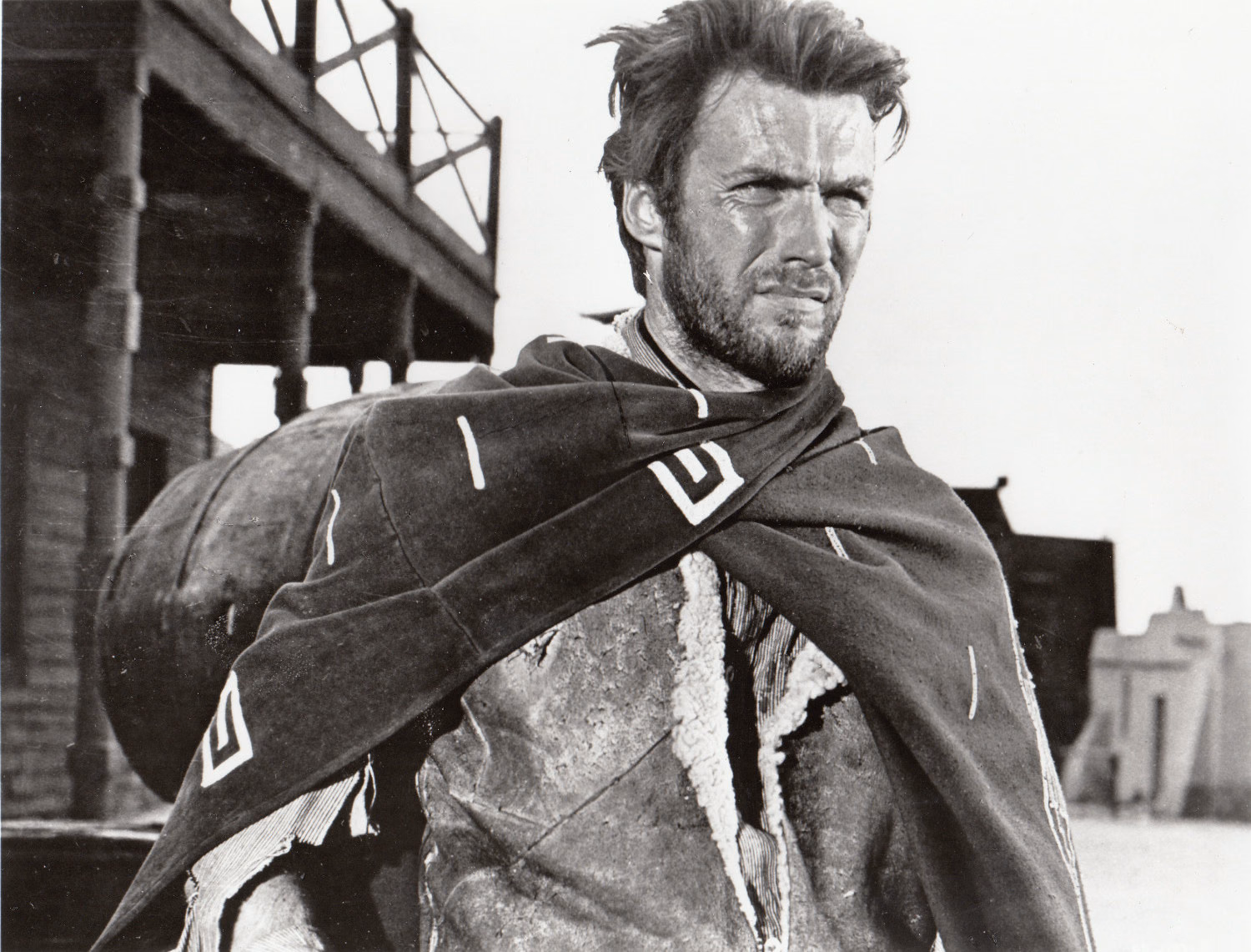 Clint Eastwood im Poncho vor einer hölzernen Fassade, Schwarzweißaufnahme